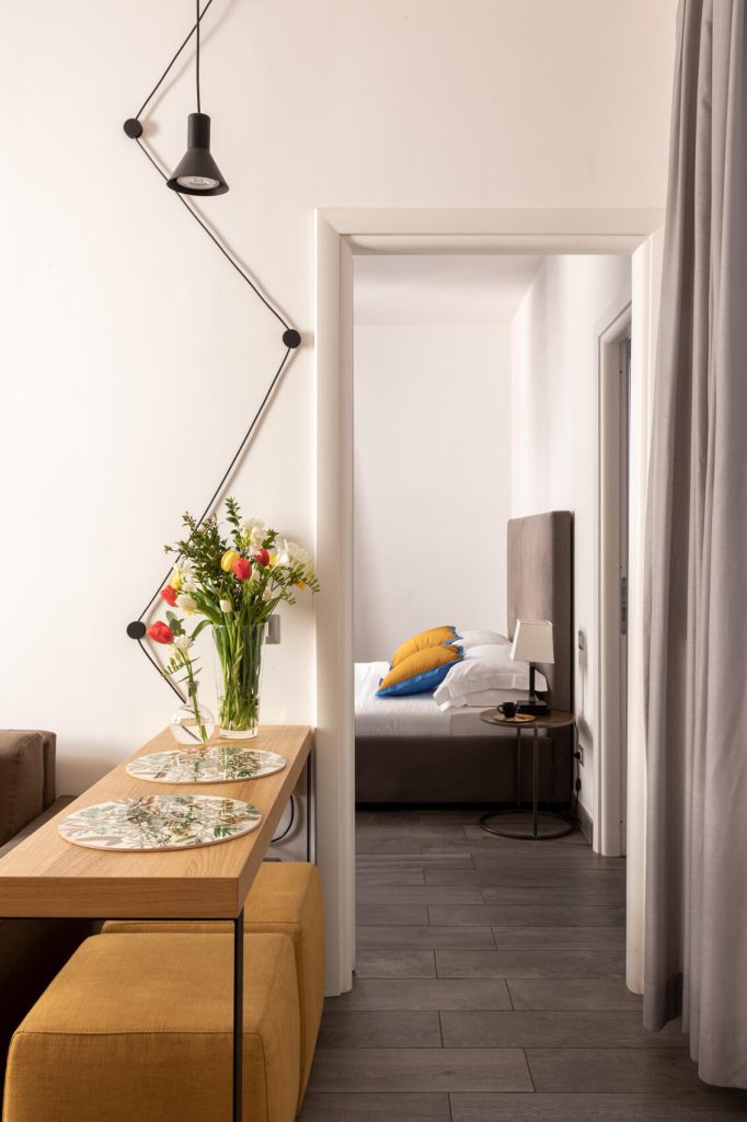 Zona living dell’Appartamento Aurora con tavolino e puff, camera matrimoniale sullo sfondo – aparthotel Roma centro