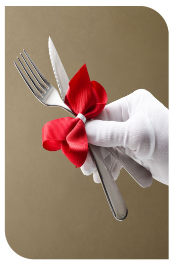 Coltello e forchetta legati con un fiocco rosso tenuti in mano