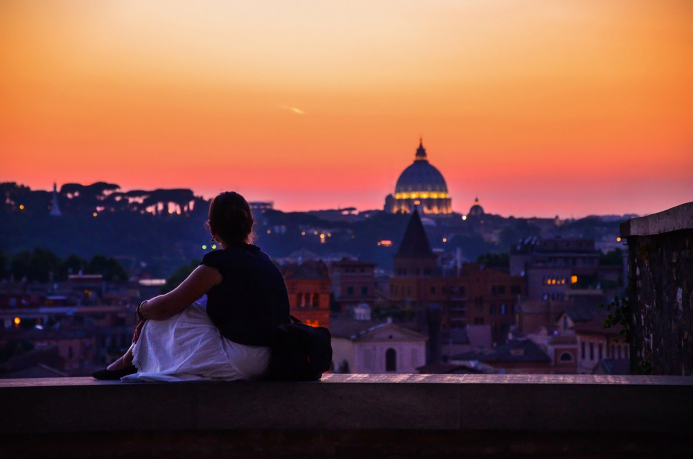 Persona che osserva Roma al tramonto con la cupola di San Pietro sullo sfondo